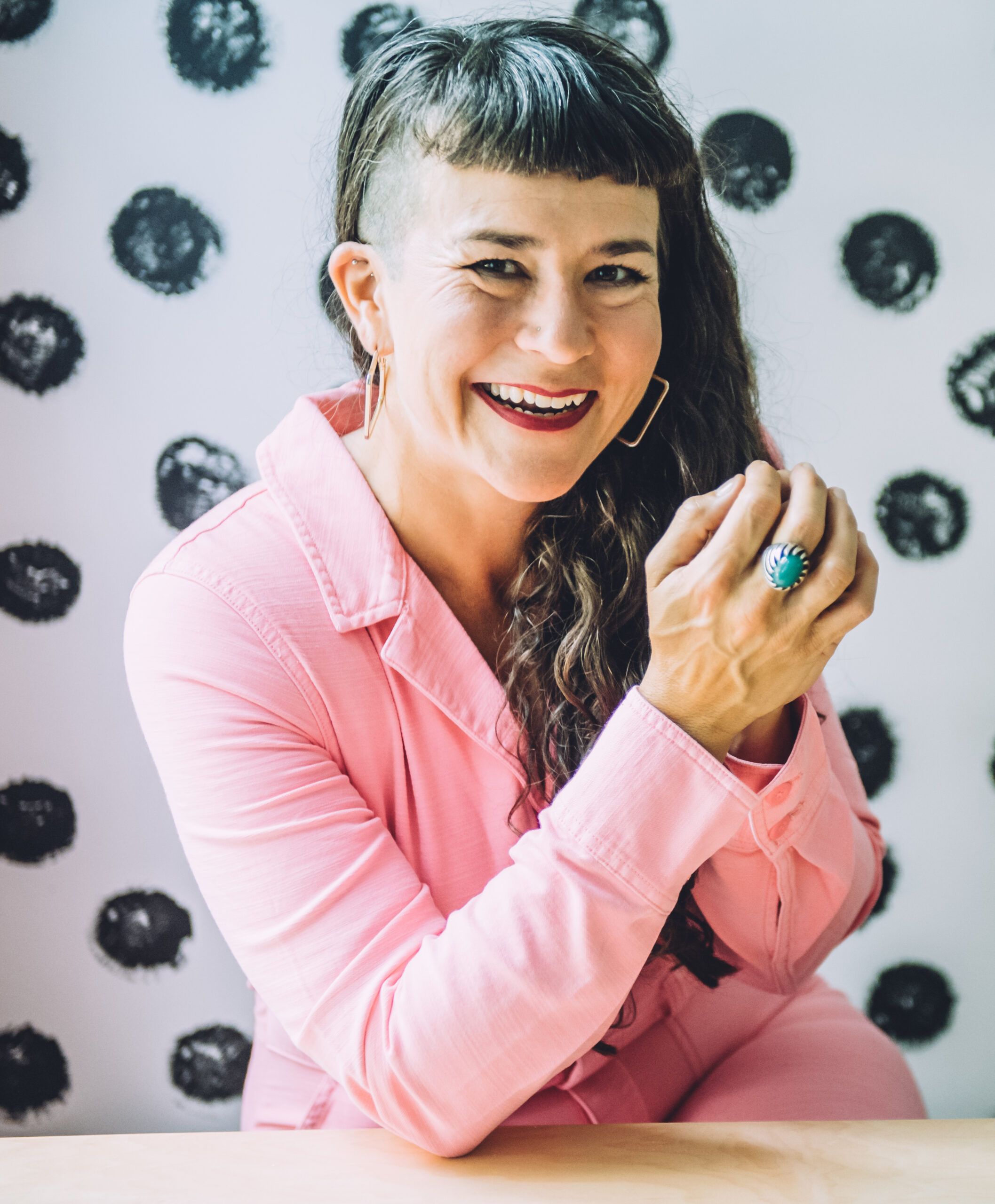 Life coach Victoria Albina in a pink jumpsuit smiling and sitting at a table