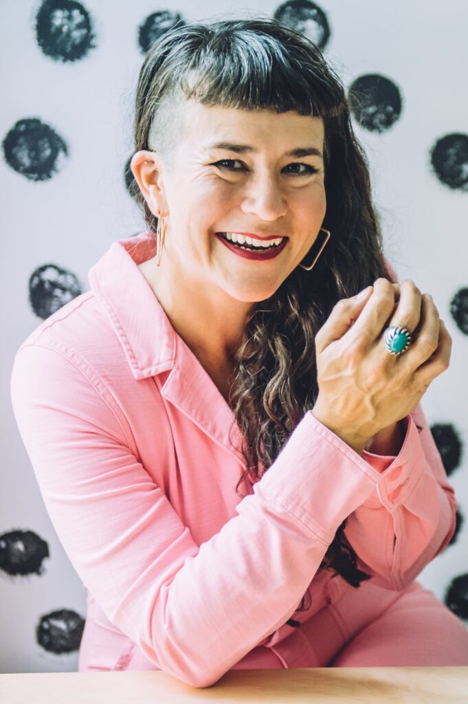 Life coach Victoria Albina wearing pink coveralls and sitting in front of a polka dot wall